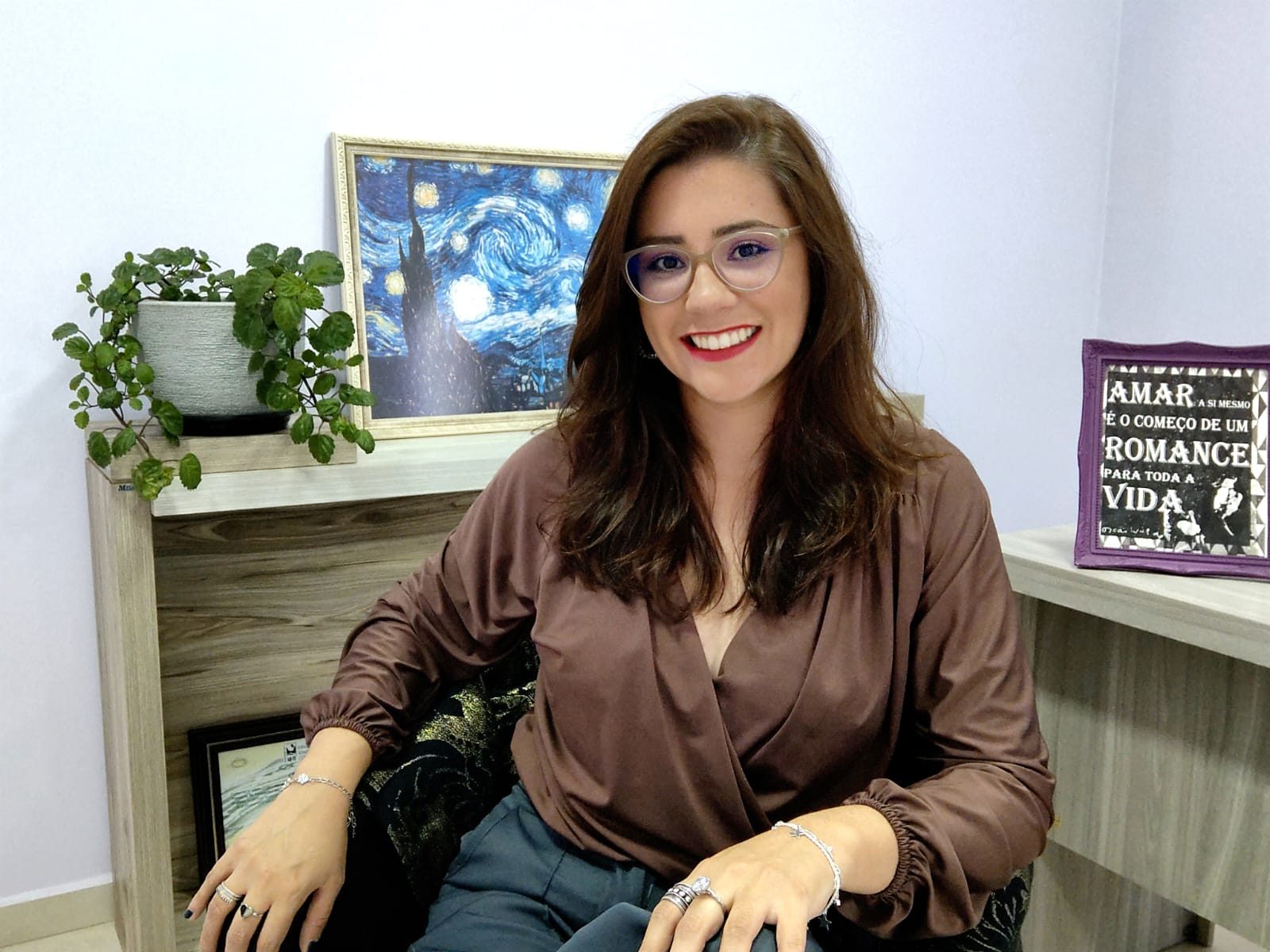 Grazieli em seu consultório, com plantas e um quadro de A Noite Estrelada